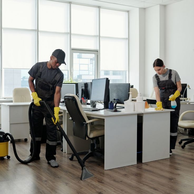 Two cleaners disinfecting desks and vacuuming in an office